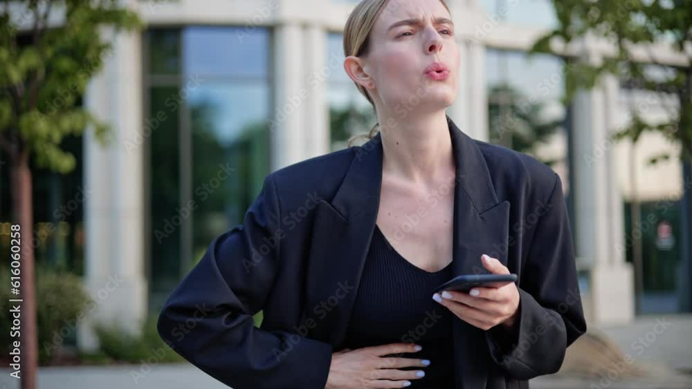 Unhappy woman feeling stomach pain, ache due to nervous before important event. Sick girl standing outdoor, holding belly, feeling abdominal or menstrual pain near office place holding mobile phone. Unhappy woman feeling stomach pain, ache due to nervous before important event. Sick girl standing outdoor, holding belly, feeling abdominal or menstrual pain near office place holding mobile phone.