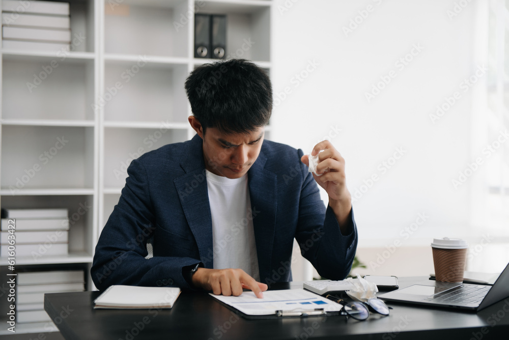 Frustrated young Asian businessman working on a laptop computer sitting at his working place in modern office Frustrated young Asian businessman working on a laptop computer sitting at his working place in modern office