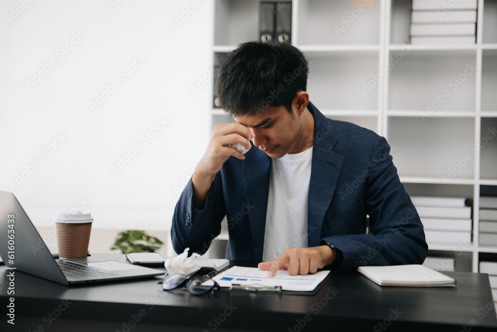 Frustrated young Asian businessman working on a laptop computer sitting at his working place in modern office Frustrated young Asian businessman working on a laptop computer sitting at his working place in modern office