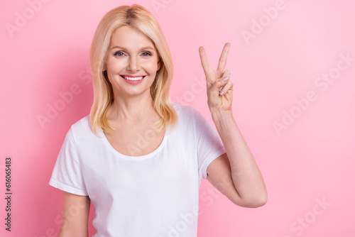Photo of adorable pensioner woman feel young showing v sign symbol wear white shirt isolated pink color background
