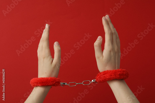 Red fluffy handcuffs on the hands on a red background
