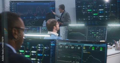Technical support specialists sit at computers with displayed blockchain network map and server data. Big data scientists work in monitoring room. Big screens on the wall. Concept of cyber security.
