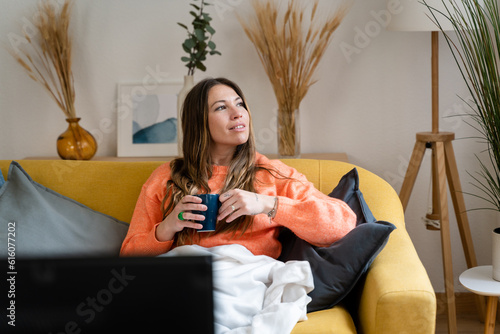 Thoughtful woman in living room drinking coffee.