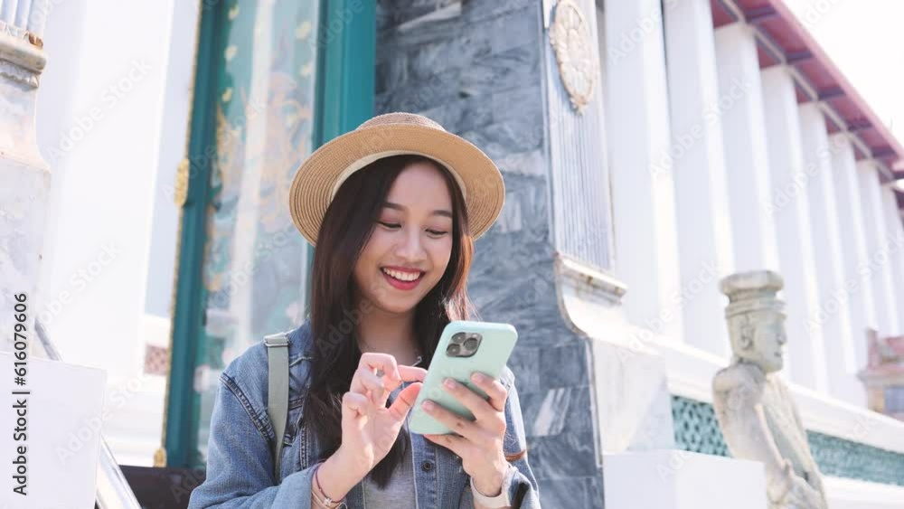 Portrait of Asian female traveler using a mobile phone on sidewalk of buddhist temple on street in Bangkok, Thailand, Southeast Asia - smart phone and internet for traveling concept