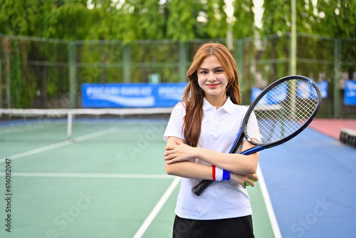 Portrait of female tennis player with racket smiling to camera confidently, showcasing her passion and determination for the game © Prathankarnpap