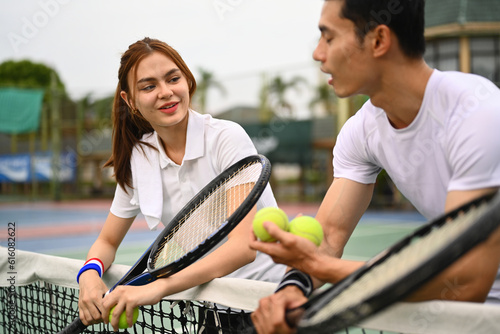Smiling sportswoman holding racket and talking with male tennis coach, standing near net on the court
