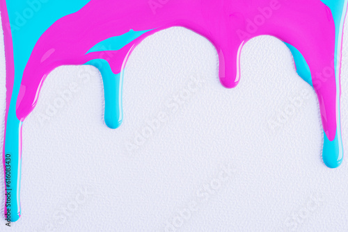 Pink and blue mixed drops of paint flow down on white canvas. Abstract art. Colorful paint dripping on the white wall