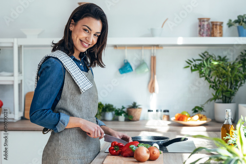 Fotografie Healthy young woman cutting fresh vegetables while cooking healthy food in the kitchen at home