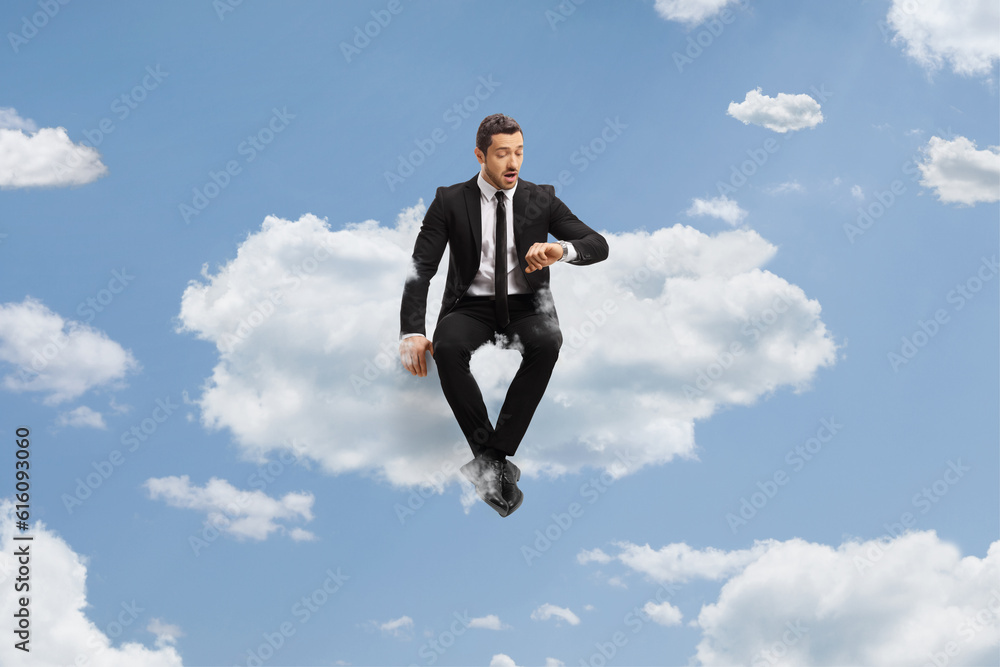 Businessman sitting on a cloud and checking time on watch Businessman sitting on a cloud and checking time on watch