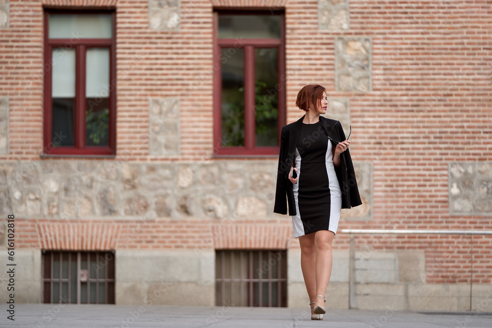 red-haired businesswoman strolling in an elegant dress and sunglasses