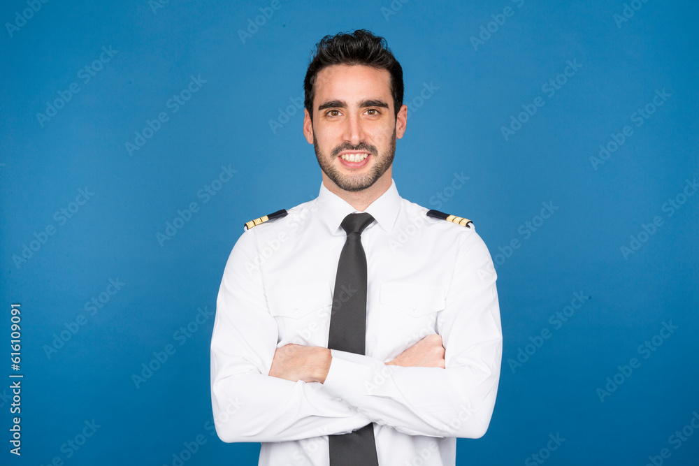 Smiling pilot in studio with crossed arms on blue background Smiling pilot in studio with crossed arms on blue background