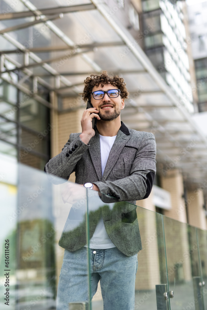 Businessman dressed in formal clothes standing outside a glass building with folder and talking on mobile phone Businessman dressed in formal clothes standing outside a glass building with folder and talking on mobile phone