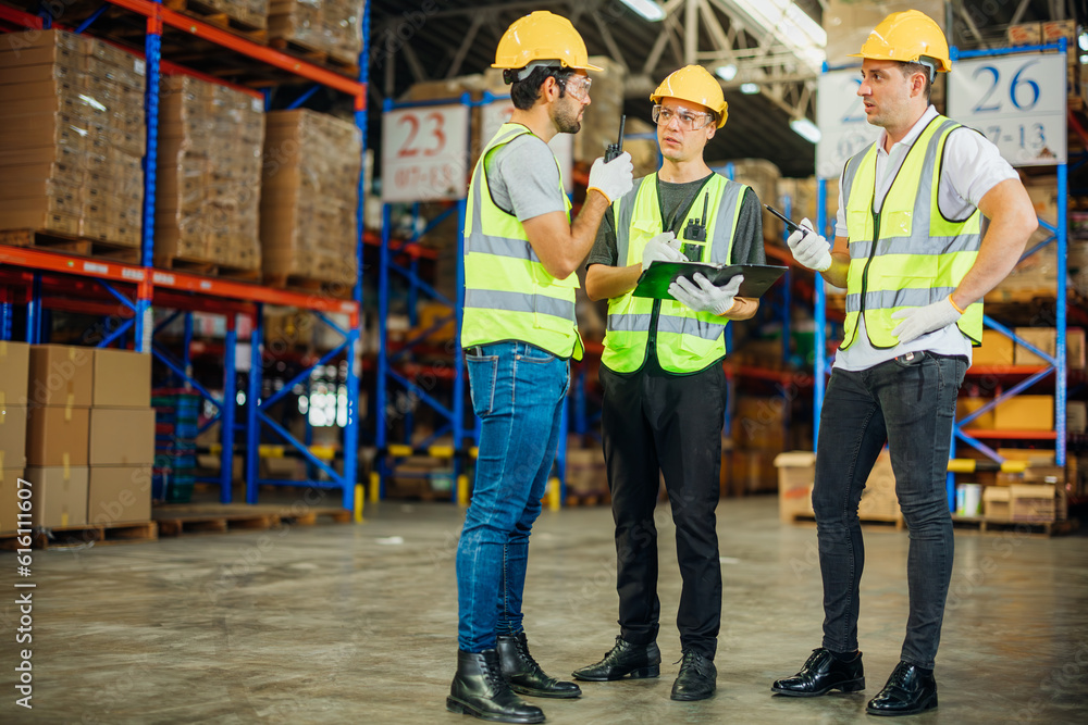 Three warehouse workers using a digital tablet while recording inventory. Logistics employees working with warehouse management software in a large distribution centre. Three warehouse workers using a digital tablet while recording inventory. Logistics employees working with warehouse management software in a large distribution centre.