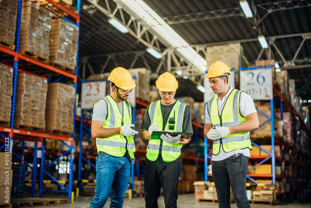 Three warehouse workers using a digital tablet while recording inventory. Logistics employees working with warehouse management software in a large distribution centre. Three warehouse workers using a digital tablet while recording inventory. Logistics employees working with warehouse management software in a large distribution centre.