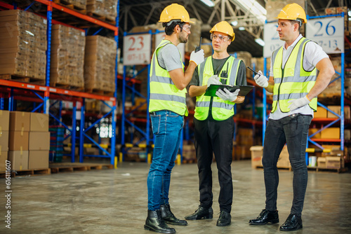 Three warehouse workers using a digital tablet while recording inventory. Logistics employees working with warehouse management software in a large distribution centre.