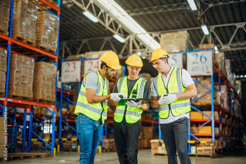 Three warehouse workers using a digital tablet while recording inventory. Logistics employees working with warehouse management software in a large distribution centre.
