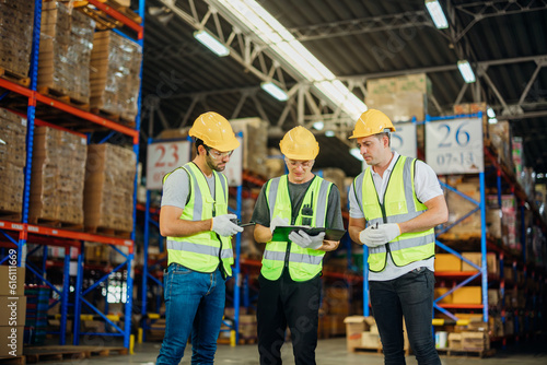 Three warehouse workers using a digital tablet while recording inventory. Logistics employees working with warehouse management software in a large distribution centre.