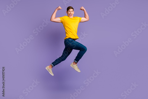Full length of attractive active guy jumping up running fists raised air isolated over violet color background