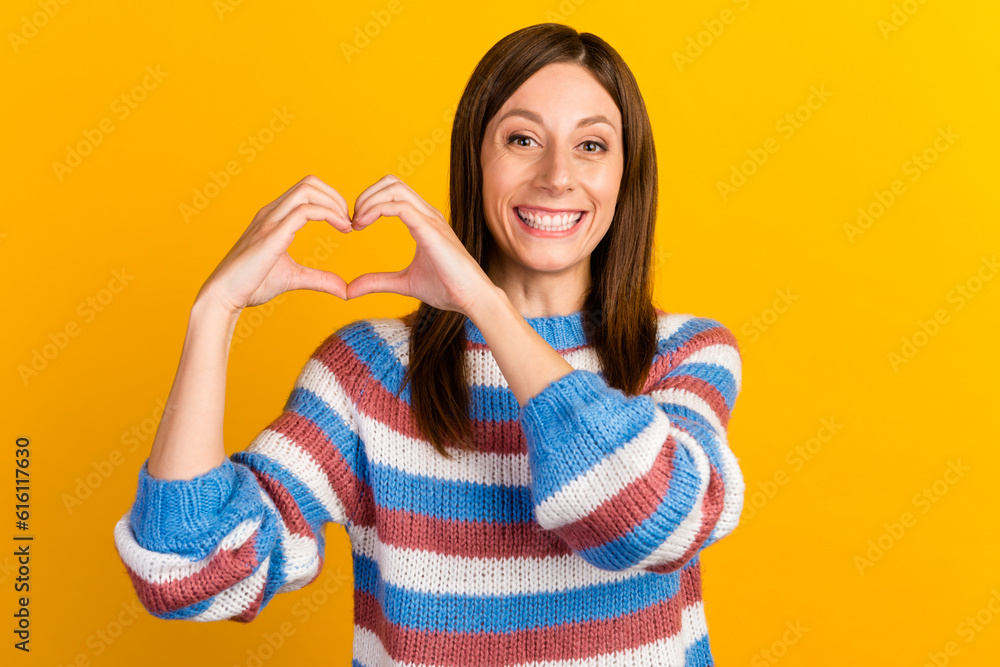 Image of young woman with long brown hair smiling and showing heart shape with fingers isolated over bright background Image of young woman with long brown hair smiling and showing heart shape with fingers isolated over bright background
