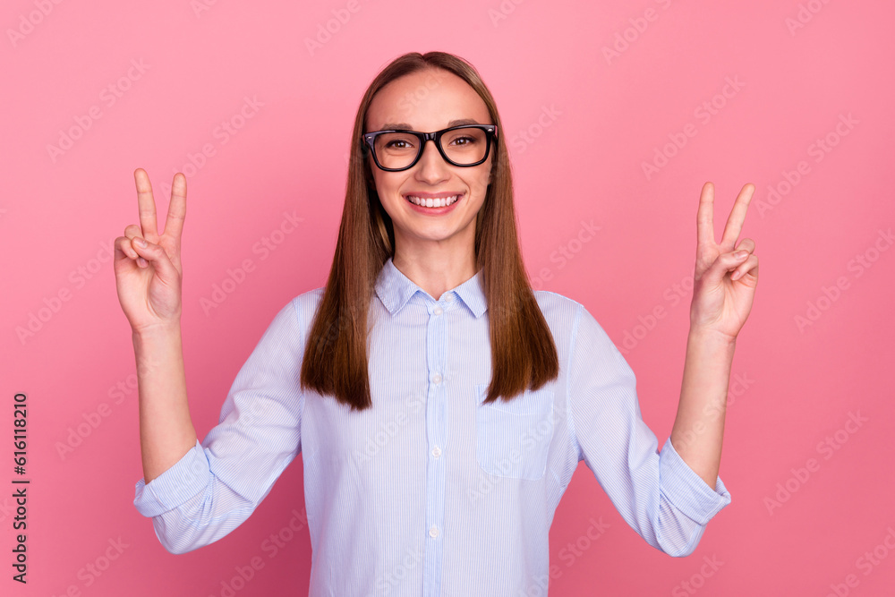 Photo of professional young girl makes peace gesture shows v sign isolated pink color background Photo of professional young girl makes peace gesture shows v sign isolated pink color background