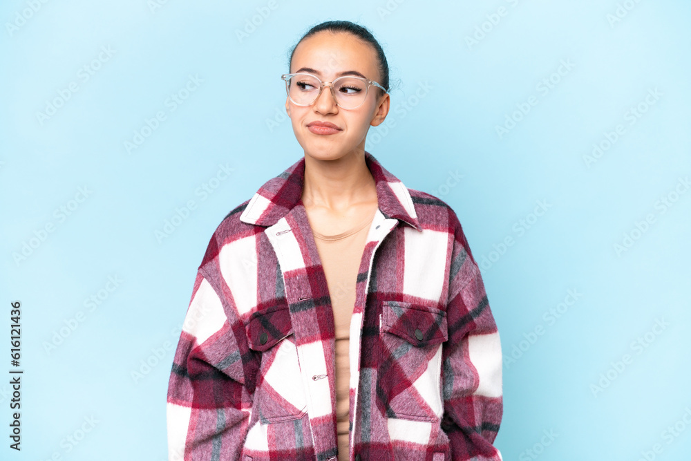 Young Arab woman isolated on blue background having doubts while looking side Young Arab woman isolated on blue background having doubts while looking side