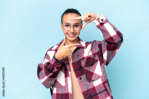 Young Arab woman isolated on blue background focusing face. Framing symbol