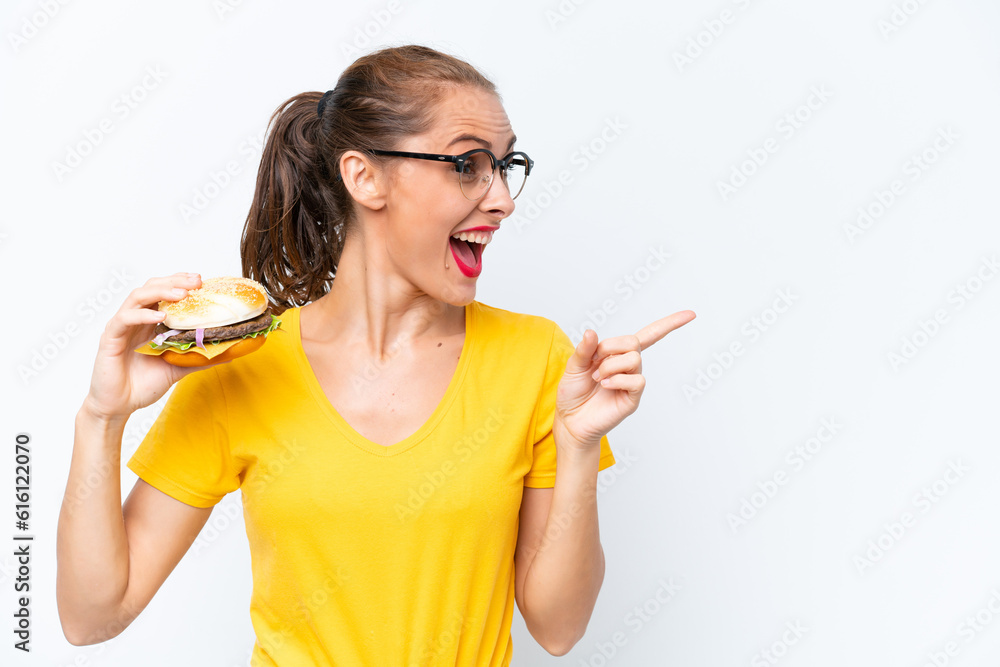 Young caucasian woman holding a burger isolated on white background intending to realizes the solution while lifting a finger up Young caucasian woman holding a burger isolated on white background intending to realizes the solution while lifting a finger up