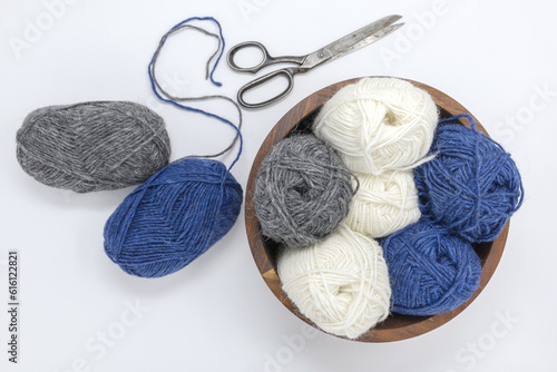 Blue grey white wool yarn balls in wooden basket and vintage scissors on a white background, stockinette stitch knitted texture in progress