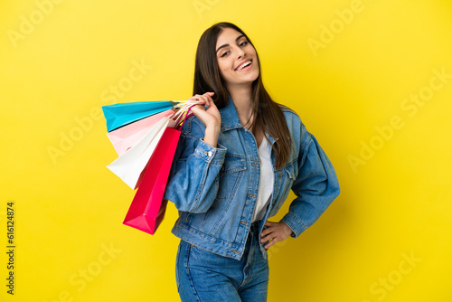 Young caucasian woman isolated on blue background holding shopping bags and smiling