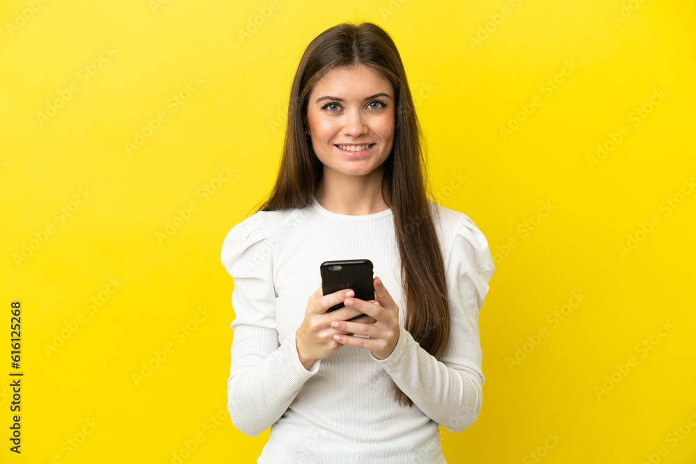Young caucasian woman isolated on yellow background sending a message with the mobile Young caucasian woman isolated on yellow background sending a message with the mobile