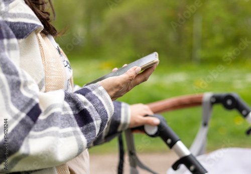 mother with baby stroller walking in park, using smartphone taking selfie.green environment.young woman maternity leave,motherhood,close up stroller parts