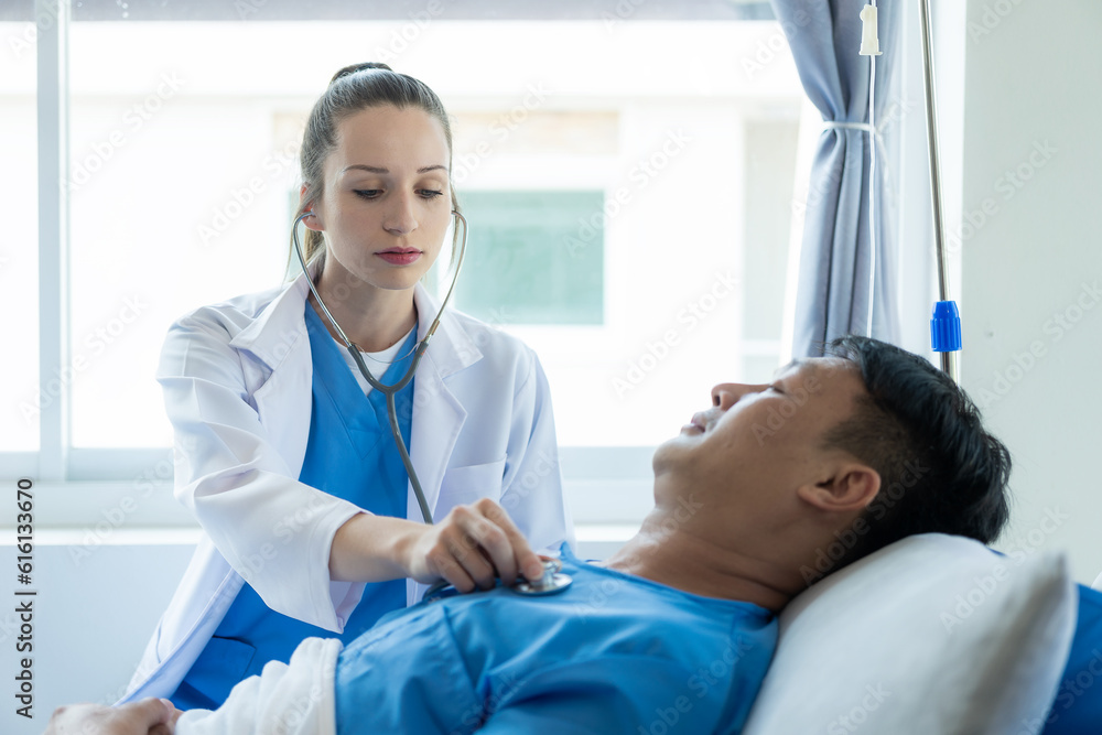Doctor and young male patient lying in bed while checking pulse Consult and explain to nurse taking notes in hospital room with saline solution, professional medical services concept Doctor and young male patient lying in bed while checking pulse Consult and explain to nurse taking notes in hospital room with saline solution, professional medical services concept