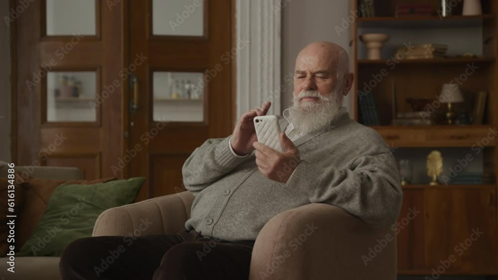 Grandfather Laughing Browsing on Smartphone in Armchair Grandfather Laughing Browsing on Smartphone in Armchair