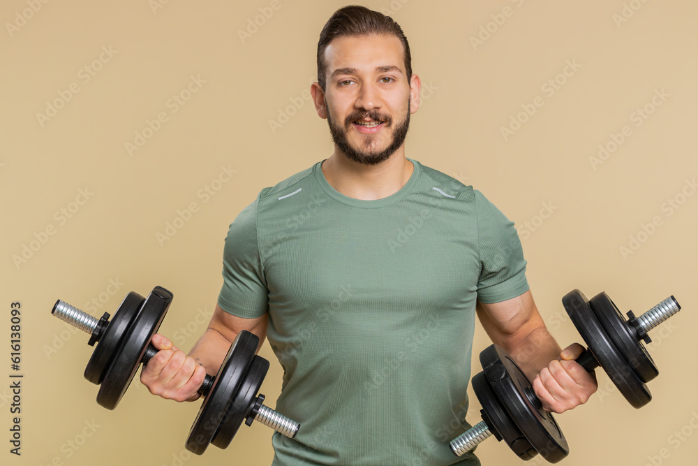 Athlete young sportive man working out. Middle eastern bodybuilder instructor sportsman guy training biceps, weightlifting dumbbells indoors on studio beige background. Strong, exercise, motivation Athlete young sportive man working out. Middle eastern bodybuilder instructor sportsman guy training biceps, weightlifting dumbbells indoors on studio beige background. Strong, exercise, motivation