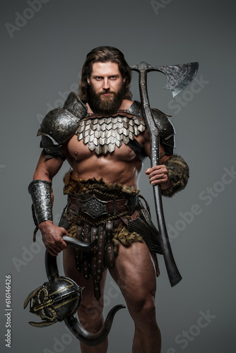 A bearded viking with long hair stands against a gray background while holding a large two-handed axe, dressed in lightweight fur-lined armor