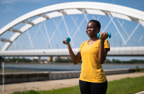 Young woman enjoys exercising with weights outdoor.  © inesbazdar