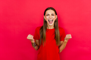 Achievement concept. Young woman in casual shirt raised fists, eyes close up isolated on red background