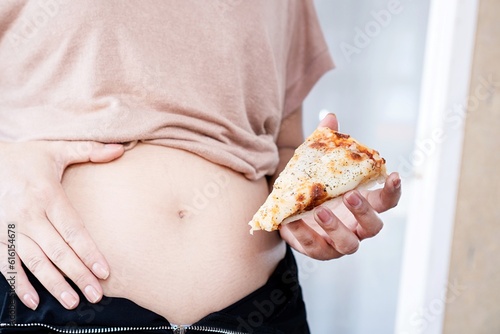 closeup woman with fat belly eating junk food   hand holding pizza  fast food effects concept
