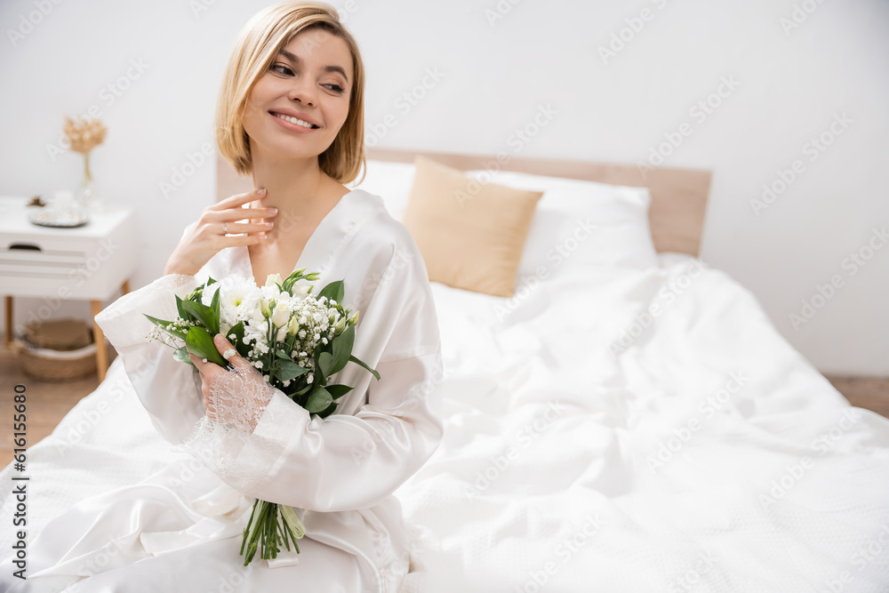 anticipation and happiness, cheerful bride with blonde hair sitting on bed and holding bridal bouquet, young woman in white robe, beautiful, excitement, feminine, blissful, wedding preparation anticipation and happiness, cheerful bride with blonde hair sitting on bed and holding bridal bouquet, young woman in white robe, beautiful, excitement, feminine, blissful, wedding preparation