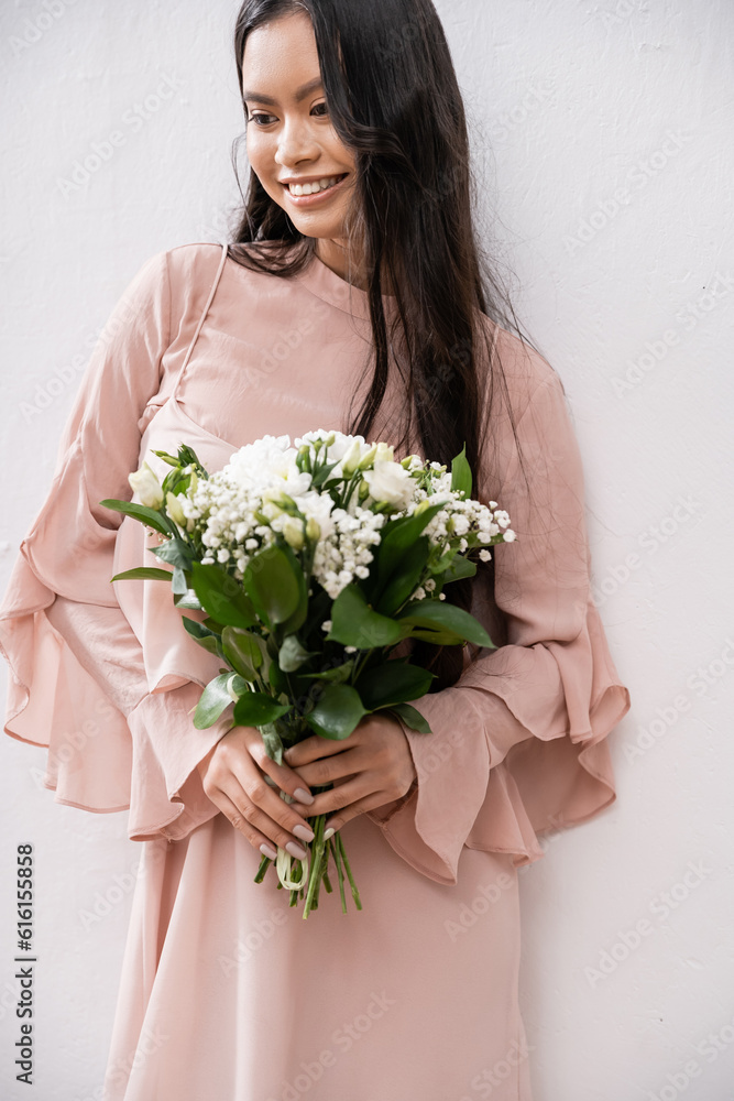 happy bridesmaid in pastel pink dress holding bouquet, asian woman with brunette hair on grey background, white flowers, special occasion, wedding, fashion, smile and joy happy bridesmaid in pastel pink dress holding bouquet, asian woman with brunette hair on grey background, white flowers, special occasion, wedding, fashion, smile and joy