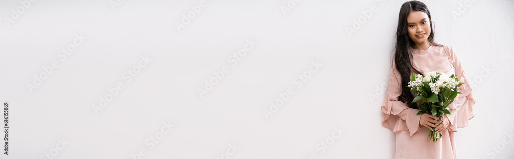 asian bridesmaid in pastel pink dress holding bouquet, happy woman with brunette hair on grey background, white flowers, special occasion, wedding, fashion, smile and joy, banner asian bridesmaid in pastel pink dress holding bouquet, happy woman with brunette hair on grey background, white flowers, special occasion, wedding, fashion, smile and joy, banner
