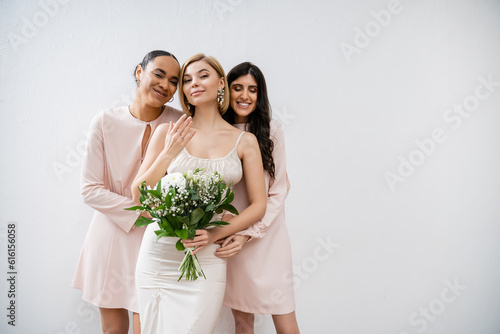 special occasion, bridesmaids hugging bride, friendship goals, grey background, happy multicultural girlfriends, cultural diversity, bridal bouquet, bridal party, blonde and brunette women