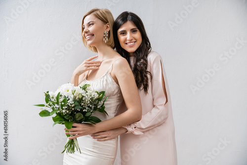 special occasion, bridesmaid hugging bride, friendship goals, grey background, cheerful girlfriends, bridal bouquet, blonde and brunette women, white flowers, happiness