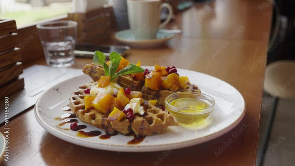 A woman puts vegetarian Viennese waffles on a table in a cafe in front of the window A woman puts vegetarian Viennese waffles on a table in a cafe in front of the window