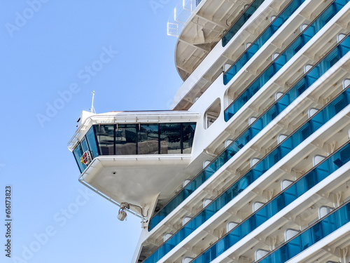 Captain's cockpit on high cruise ship. Looking up on high nautical vessel from port on a sunny day. Many hotel rooms with sea view balconies, seperated by blue glass. Adventure travel destinatination