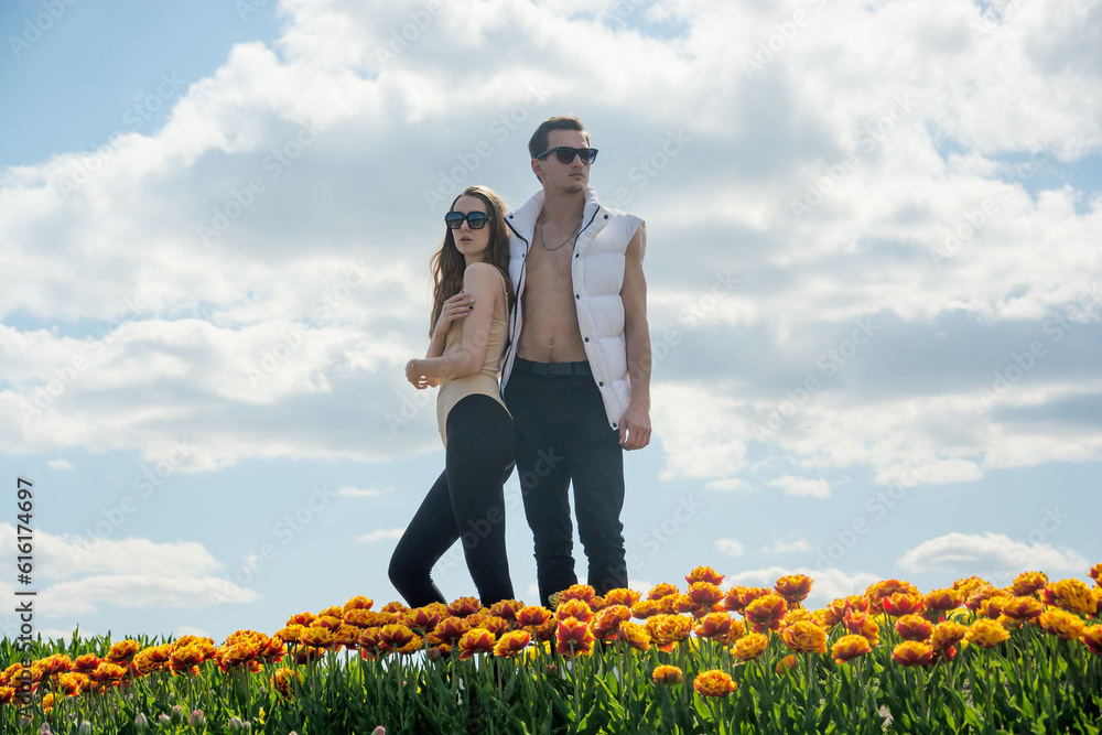 A beautiful young couple, fashion models stands in sportswear at the background of a field of colorful tulips.
