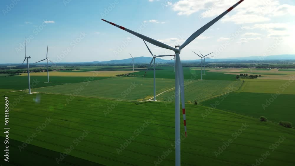 Group of windmills for electric power production in the green field against a blue sky. Aerial view of a large eco-energy wind farm. Environmental protection, renewable energy sources. 4k footage Group of windmills for electric power production in the green field against a blue sky. Aerial view of a large eco-energy wind farm. Environmental protection, renewable energy sources. 4k footage