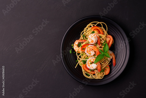 Stir-fried spaghetti or stir-fried noodles Tomato sauce and prawns on a black plate On a wooden table background. Top view.