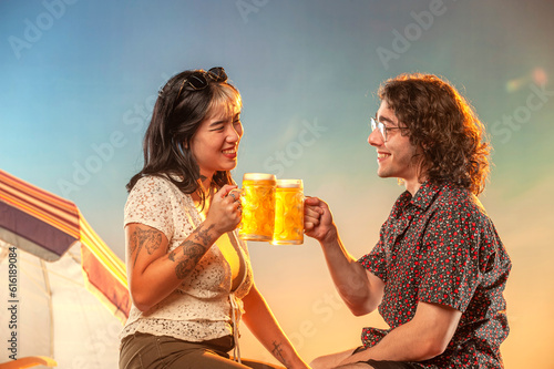 Interracial couple toasting draft beer against the sunset.