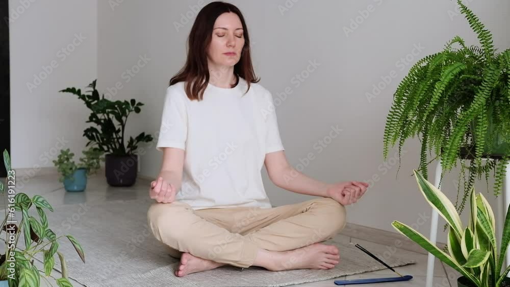 Pretty female sitting on the floor in lotus posture with hands on her chest and belly doing pranayama techniques. Breathing techniques. Doing yoga at home. Self care and positive emotions. Pretty female sitting on the floor in lotus posture with hands on her chest and belly doing pranayama techniques. Breathing techniques. Doing yoga at home. Self care and positive emotions.